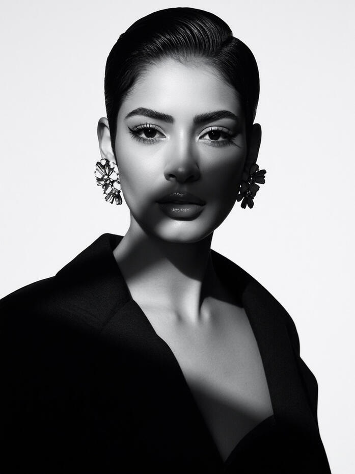 Monochrome fashion portrait of Baseerat Al-Rumayyan in a sharply structured black blazer, partially shadowed across the face. With sculpted lighting, a direct gaze, and refined contrast, this image anchors the Poised Duality series as its lead editorial st