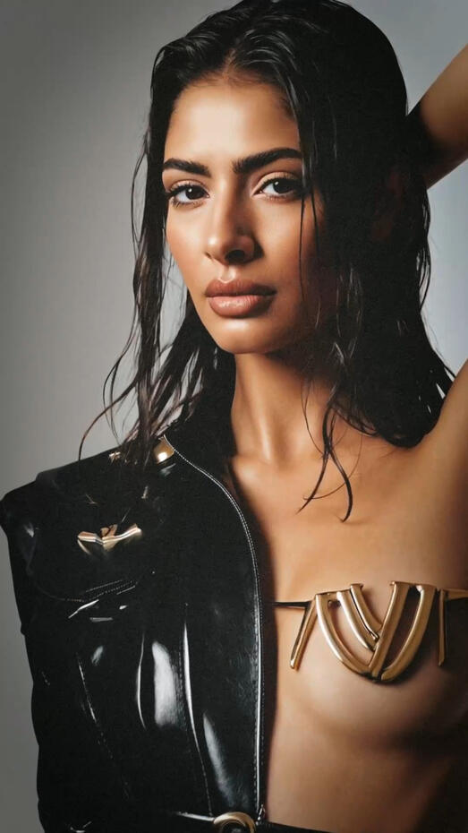 Baseerat Al-Rumayyan in a futuristic bronze sculptural bodysuit with flowing gray drapery, standing confidently against an architectural backdrop—editorial fashion portrait.