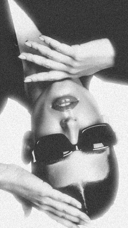 Baseerat Al-Rumayyan wearing a futuristic bronze metallic bodysuit, standing confidently with flowing hair framed by soft gray drapery, exuding high-fashion editorial elegance